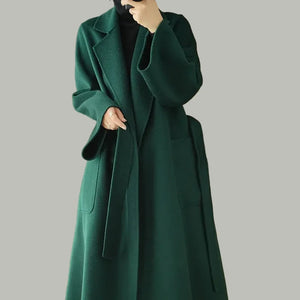 Person wearing a long green coat in a room with wooden walls and a beige chair.